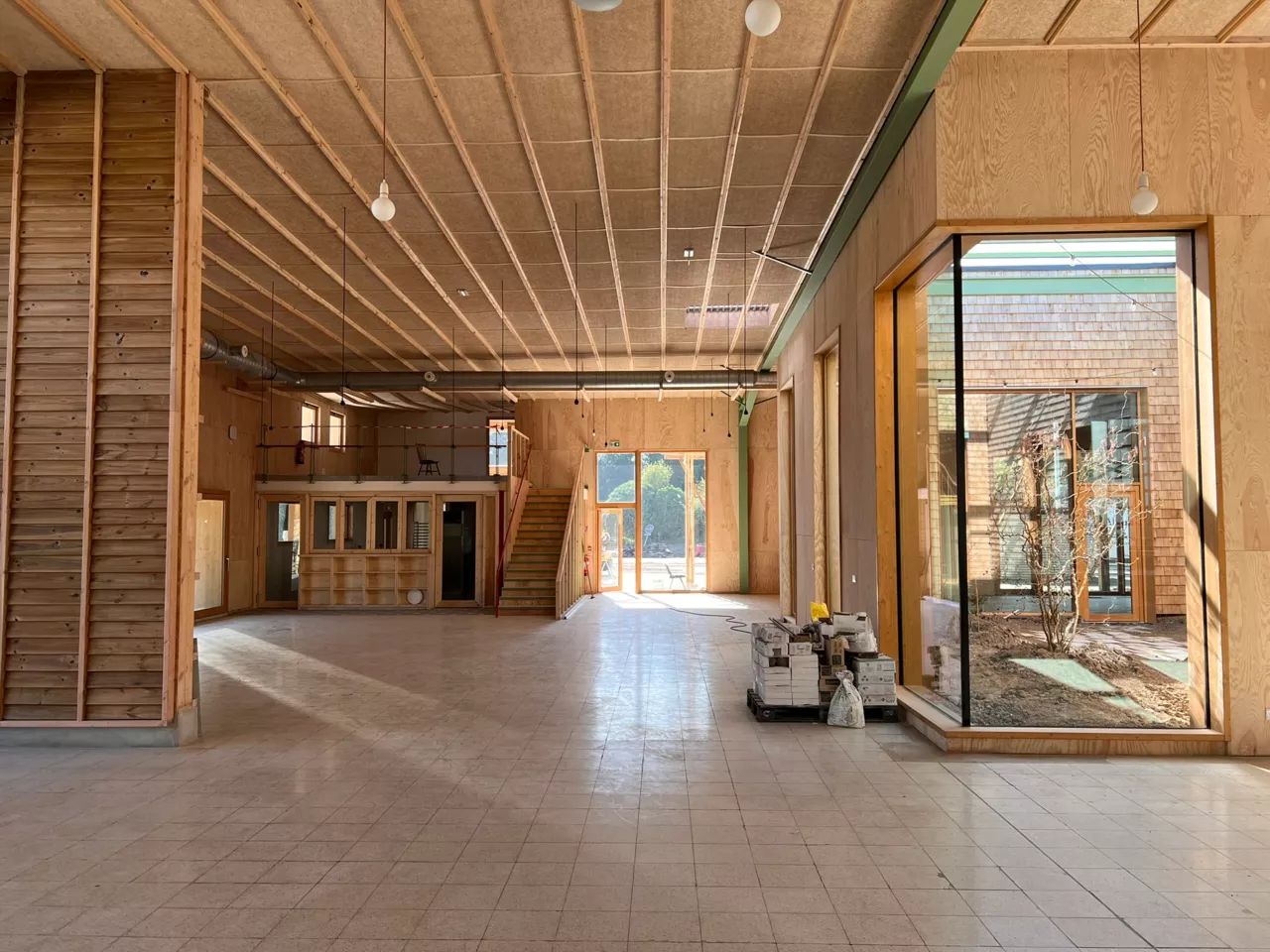 Vue intérieure du bâtiment démonstrateur de Noeux-environnement, mettant en valeur un vaste volume en ossature bois et matériaux biosourcés, avec de grandes ouvertures vitrées donnant sur le patio central.