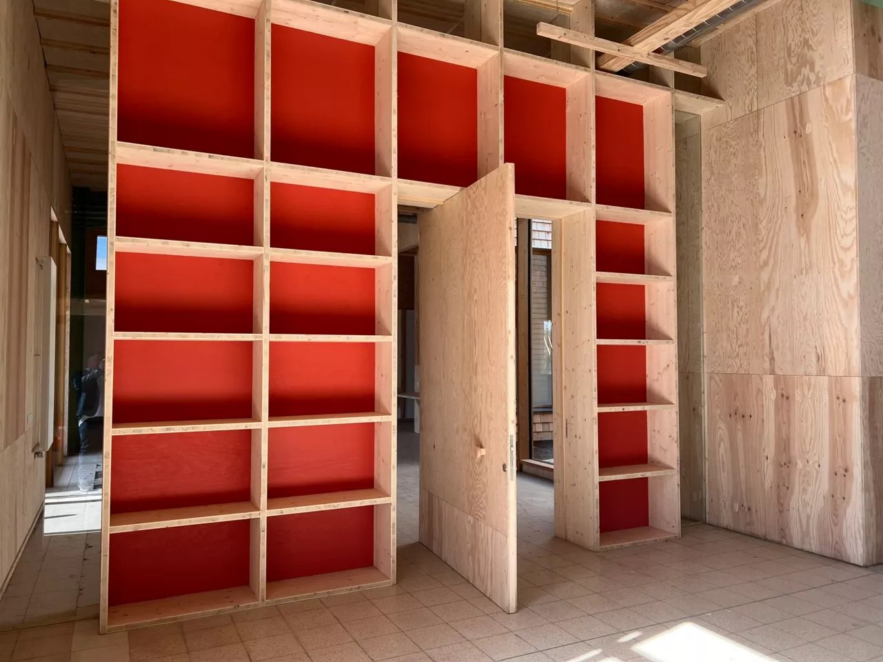 Porte pivotante intégrée dans une bibliothèque en bois sur le chantier démonstrateur de Noeux environnement, illustrant un aménagement intérieur sur mesure en matériaux biosourcés.